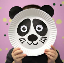 Paper plate decorated to look like a panda bear's face, held in front of a child's face