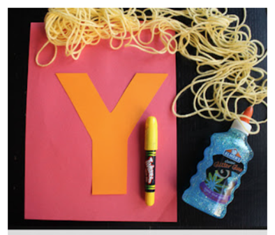 Pink construction paper with Y cut out of yellow construction paper glued on top. Yarn arranged to look like spaghetti noodles above it.