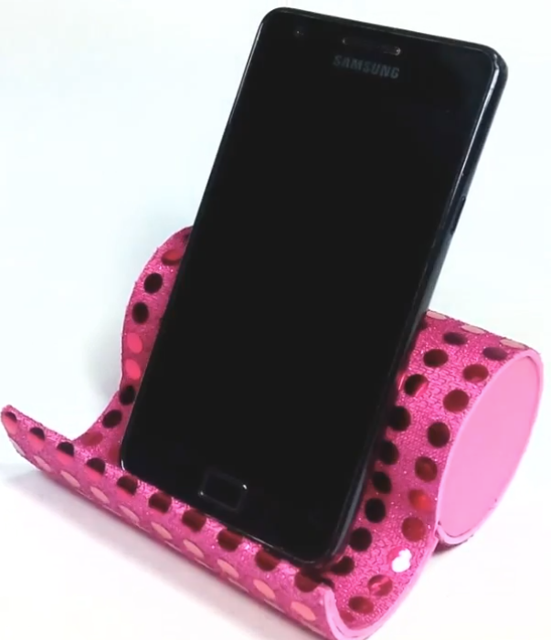 Cylindrical tube decorated with pink sequined paper, folded over to hold a small cell phone upright