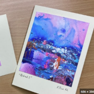 A polaroid style photo placed on a wooden surface. The artwork is shades of blue, pink, and purple.
