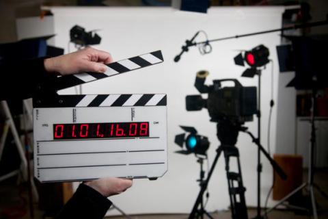 A black film camera and a hand with an open film clapper