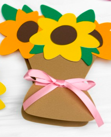 A photo of a brown paper vase with yellow sunflower and pink ribbon for added decoration. 