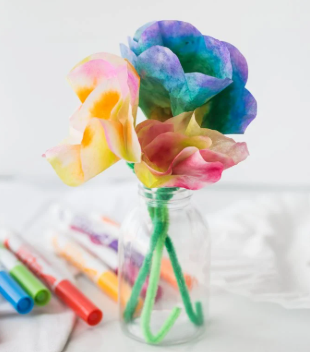 This is a picture of coffee filters that have been painted, folded, attached to pipe cleaners, and placed in a jar to resemble colorful flowers.