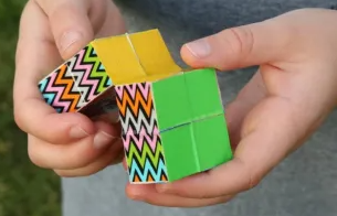Hands folding a brightly colored (yellow, green, and rainbow-striped) cube toy