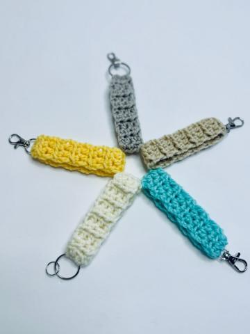 This picture is of five crocheted keychains arranged to look like a star, or asterisk. Each is a different color: yellow, white, blue, green, and grey.