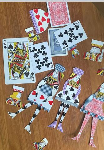 Playing card dolls (flat paper dolls made of playing cards) and regular playing cards against a brown background