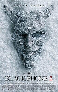 A chilling horror movie poster for Black Phone 2 shows a cracked, stone-like mask with hollow eye openings and a sinister grin embedded in an icy, textured background. The mask appears partially frozen and emerging from the surface. Text at the top reads “Ethan Hawke,” and the title “Black Phone 2” appears near the bottom along with film credits.