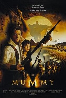 A dramatic adventure movie poster for The Mummy shows a man and woman standing in the foreground holding weapons, including a rifle, in a desert setting. Behind them, a large glowing sun illuminates a shadowy figure with outstretched arms. Pyramids, sand dunes, and a group of people on camels appear in the background. The title “The Mummy” is displayed near the bottom along with film credits.