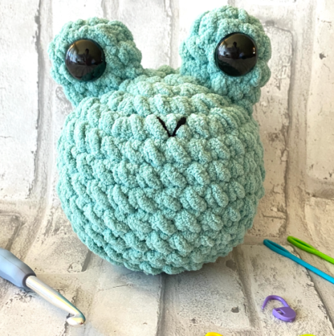 This photo is of a crocheted frog that was made from green yarn. 