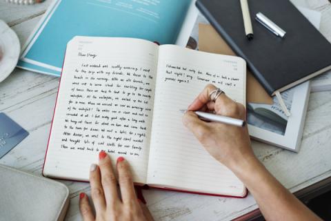 An image of a journal with hands writing in it.
