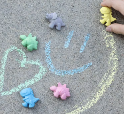 This picture is of multicolored sidewalk chalk that is in the shapes of different dinosaurs. 