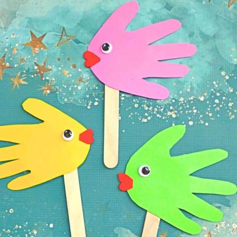 a photo of pink, green, and yellow handprint fish with googly eyes and popsicle sticks