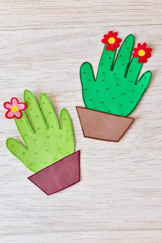 a photo of two green handprints decorated to look like cacti in a brown paper pot