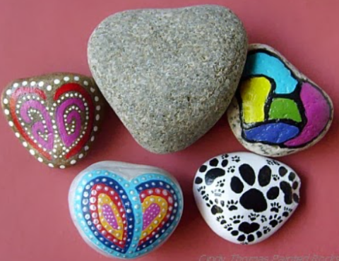 This picture is of 5 rocks, four of which are painted in bright, abstract designs.